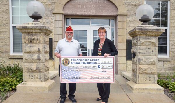 A person with an American legion cap, Dennis Soppe, presents a large check with an American flag background to UIU President Kathy Franken on the right.