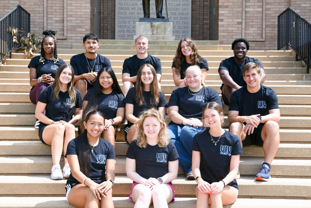Thirteen RA members in matching black shirts pose on outdoor steps