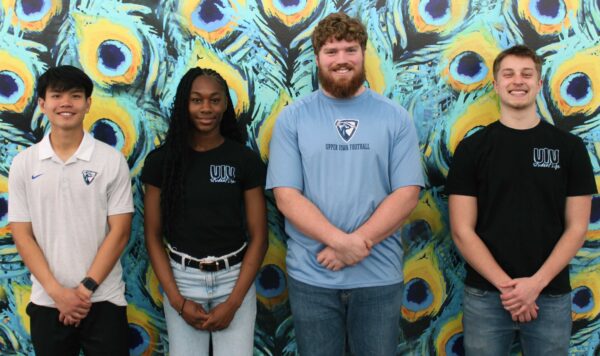 The 2026–27 SGA Council poses in front of a colorful peacock-feather mural on campus, with four student leaders standing side by side and smiling at the camera.