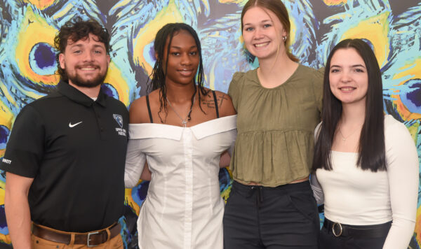 Group of UIU students posing in front of a wall with vibrant peacock graphics