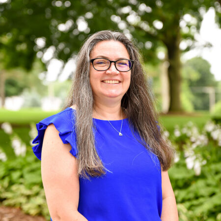 A photo of Nikki Battle with a green patch of of plants and trees in the background