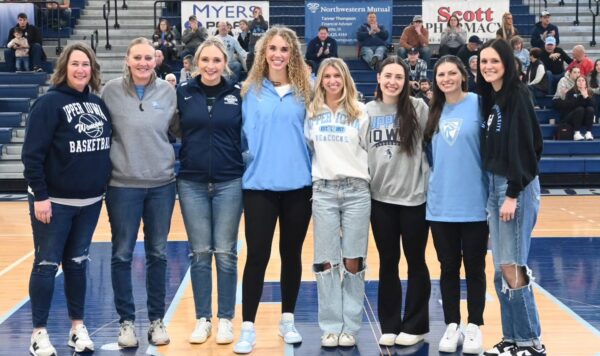 Women's basketball alumni's standing for a photo in the gym.
