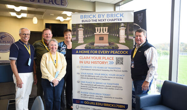A group of people pose for a photo around a large banner announcing the launch of the "Brick by Brick" campaign