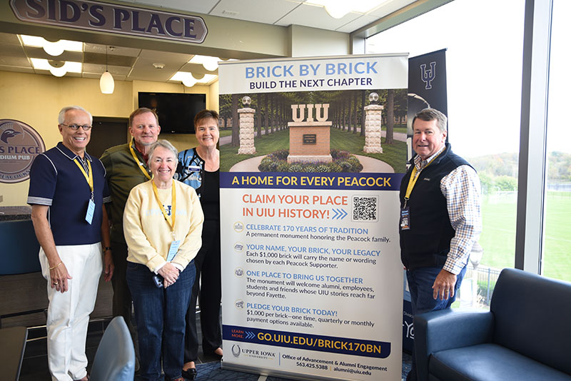 A group of people pose for a photo around a large banner announcing the launch of the "Brick by Brick" campaign