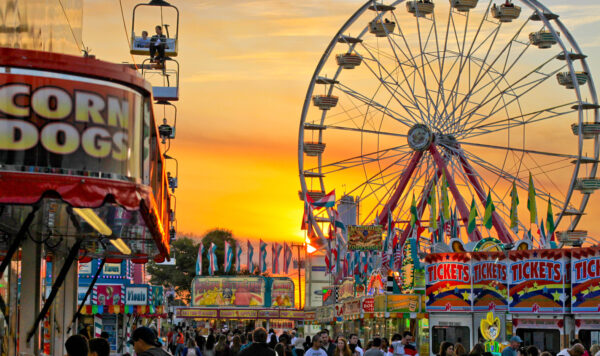 Ferris wheels, corn dogs, and a state fair crowd in front of a beautiful sunset