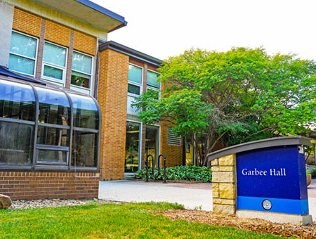 A brick building with lots of windows, with grass, trees and bike racks out front on UIU's Fayette Iowa Campus