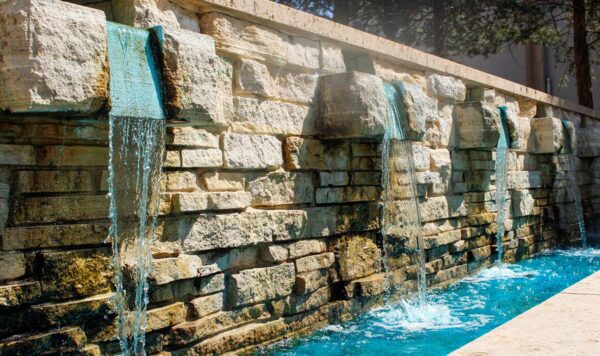 A water feature with blue water pouring over a decorative limestone wall