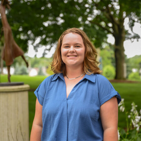 Photo of Katie Bevers outside with trees, greenery and a modern art sculpture in the background