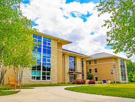 A beautiful sand colored brick building with a large rectagular window reflecting the blue sky