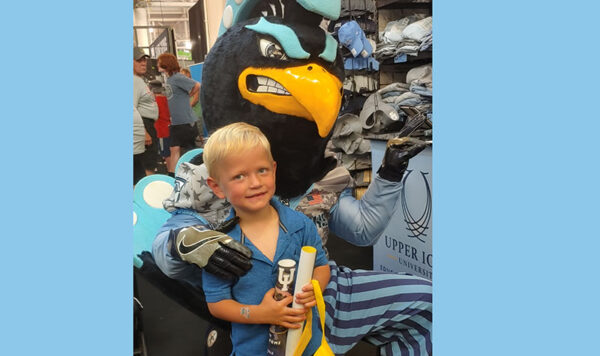 Pete the Peacock, UIU's mascot, and a young person holding a UIU poster pose for a photo at the Iowa State Fair