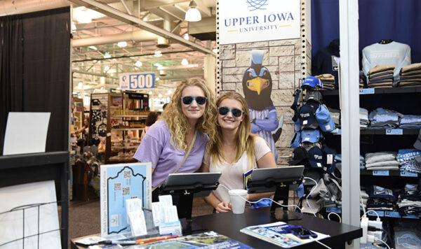 Two students wearing peacock blue sunglasses visit UIU's Iowa State Fair booth