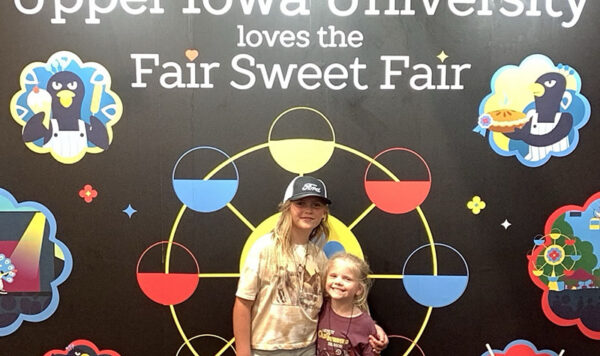 Children pose for a photo in front of a Upper Iowa University backdrop
