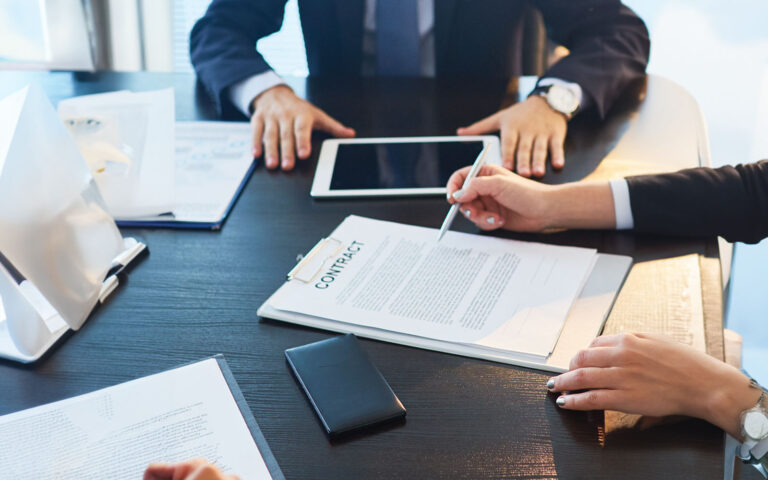 A group of leaders in business attire gather around a table to review a contract