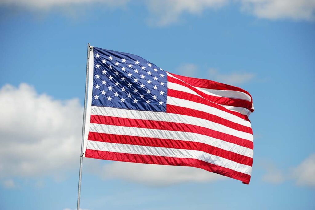 The U.S. flag waves in front of a blue sky with a few puffy clouds