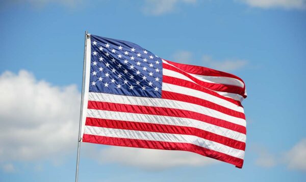 The U.S. flag waves in front of a blue sky with a few puffy clouds