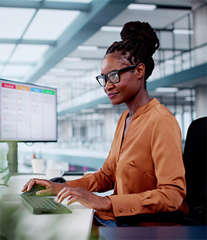 A woman works at their desk typing on a keyboard with a kanban layout displayed on their computer monitor