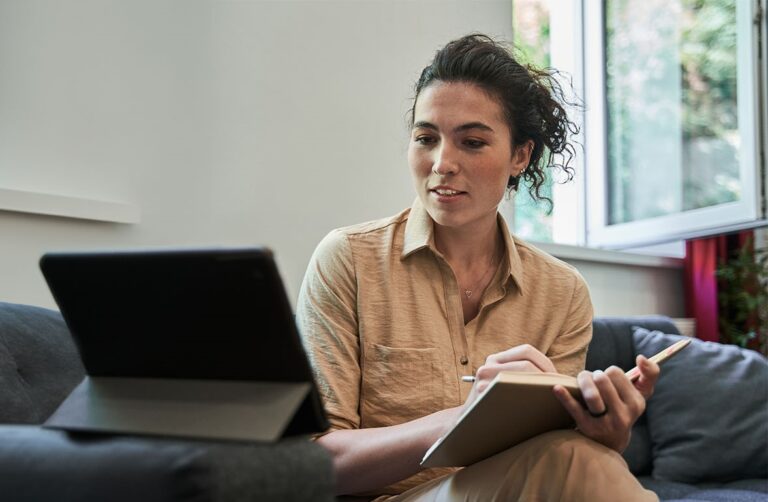 Woman in tan shirt studying on couch with laptop